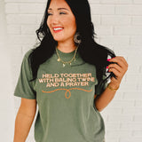 Moss green short sleeved rounded neck graphic tee that reads " Held Together With Baling Twine And A Prayer."