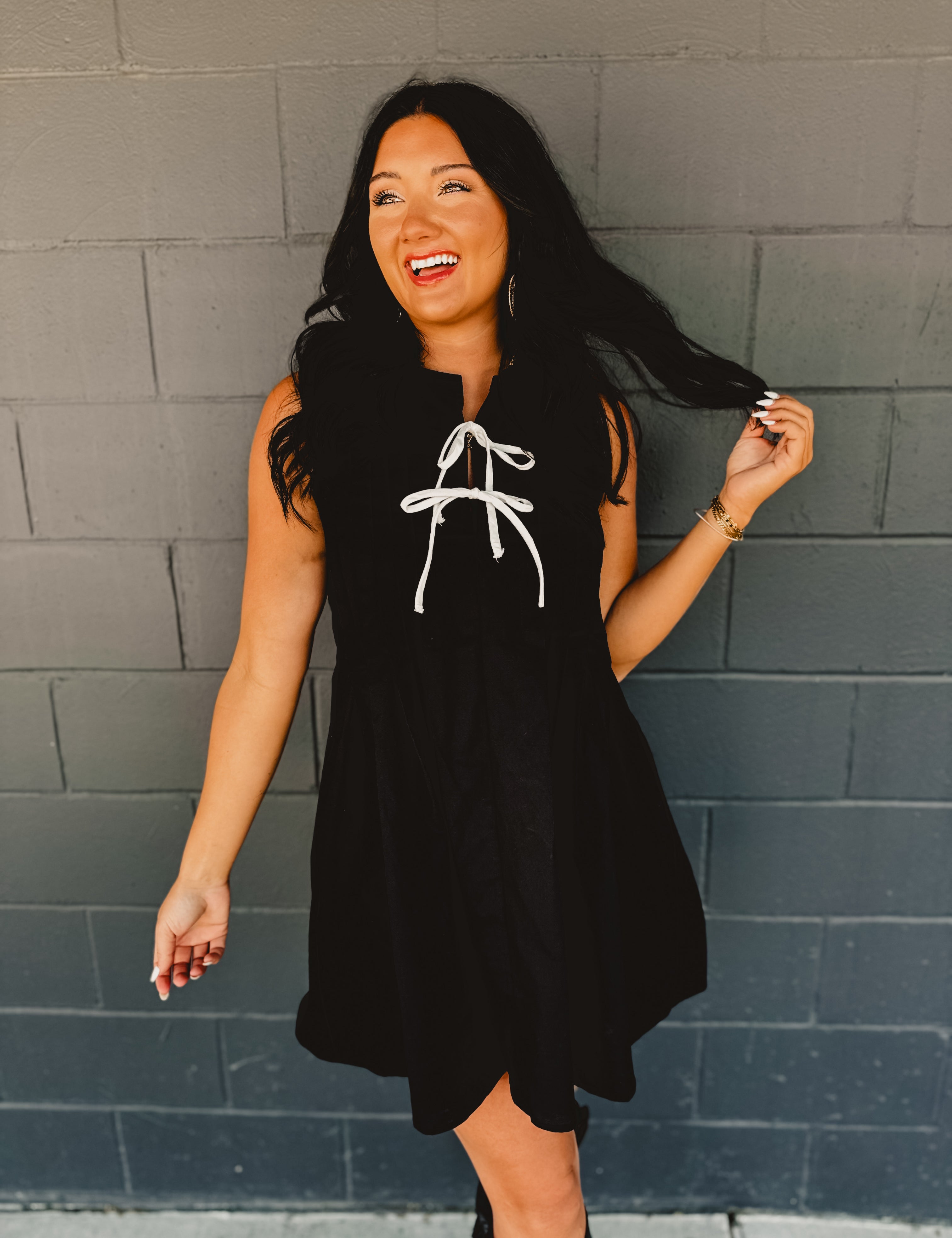 Sleeveless pleated black mini dress with white bow tie details.