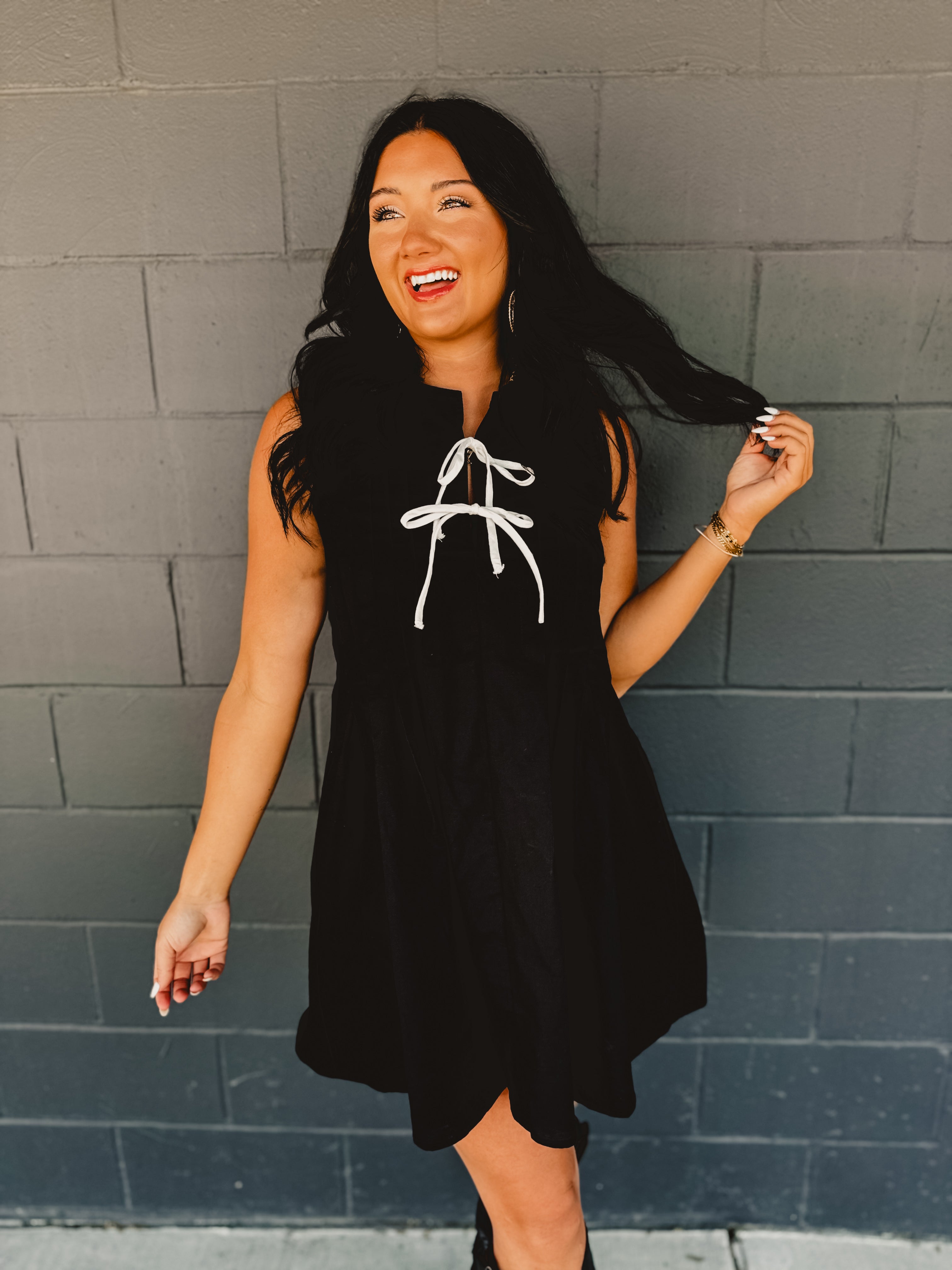 Sleeveless pleated black mini dress with white bow tie details.