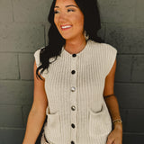 Sleeveless chunky button sweater vest with front pockets and a round neck in cream.