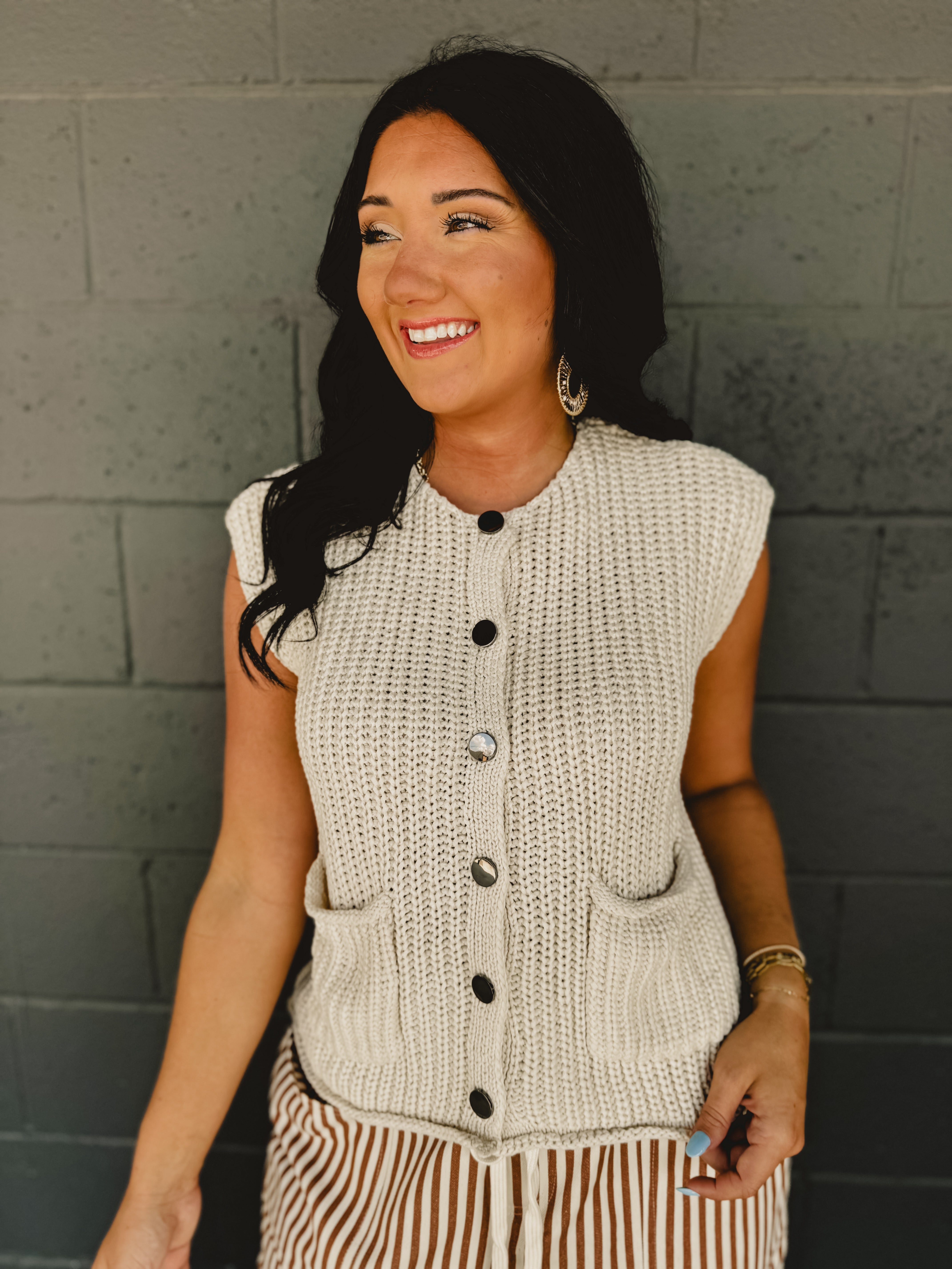 Sleeveless chunky button sweater vest with front pockets and a round neck in cream.