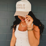Two-toned one size baseball cap reading "Cool It Cowboy" in a cream and beige color.