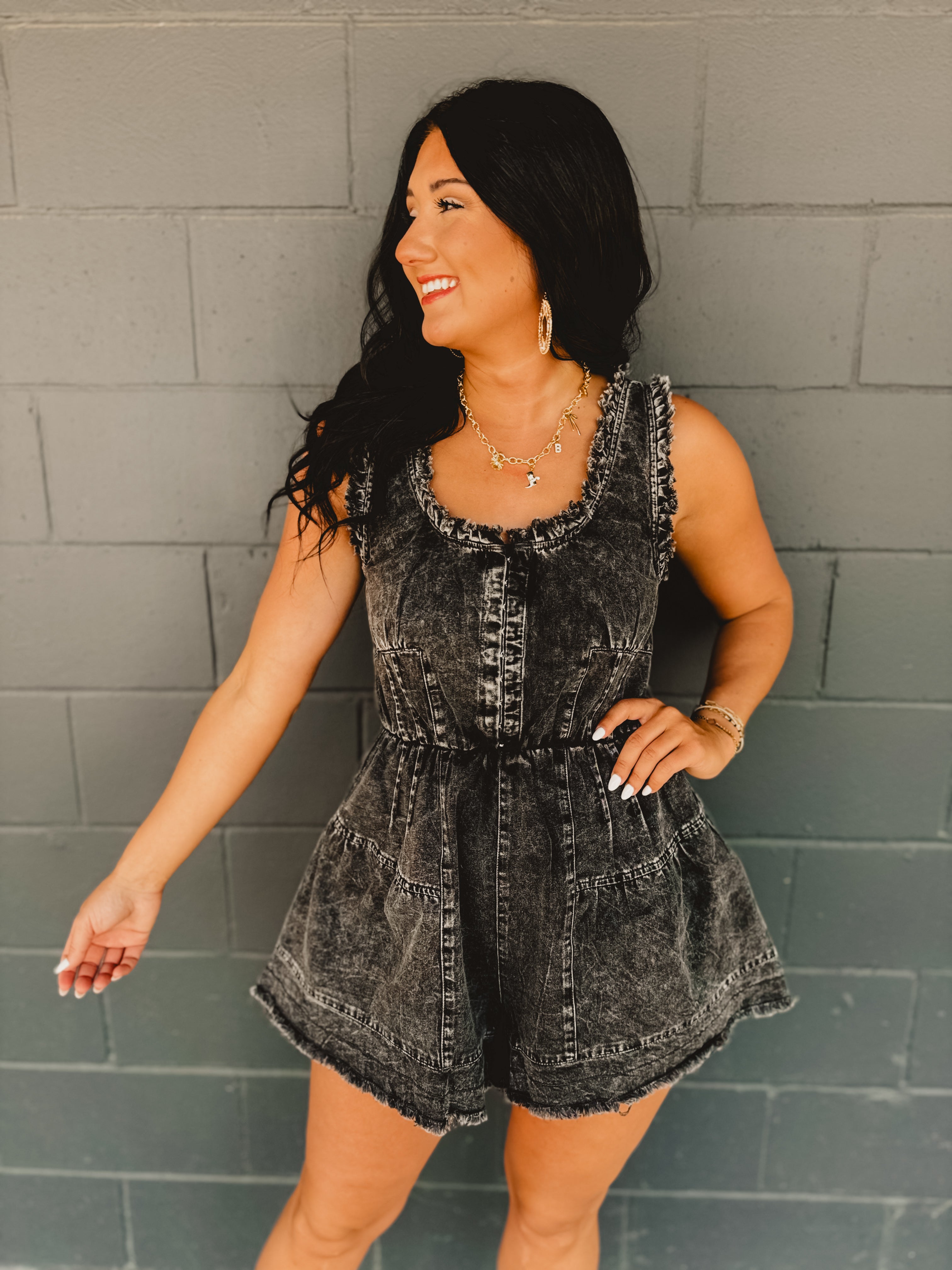 Frayed edge distressed sleeveless denim romper in acid wash black with metal clasp detail and cinching at waist.