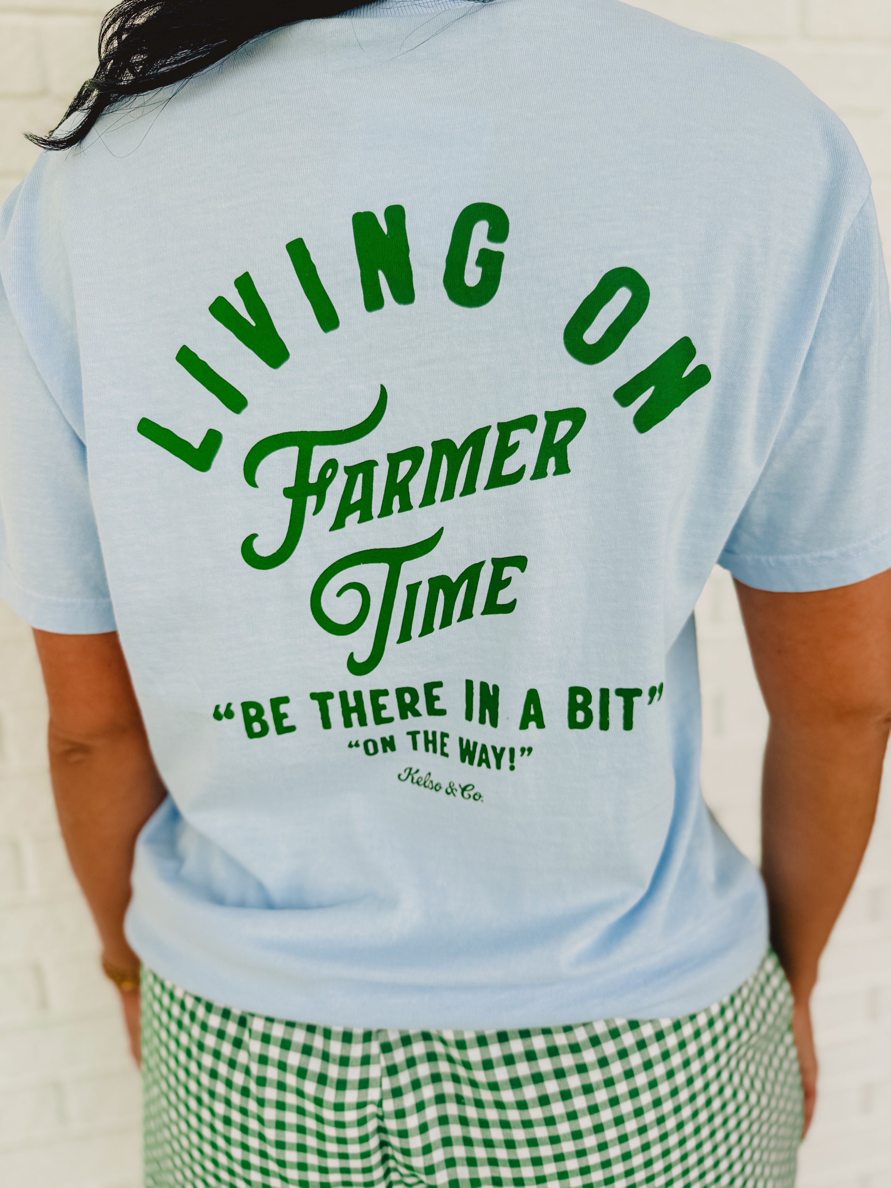 Light blue "Living On Farmer Time" short sleeved graphic tee with a round neck and green writing.