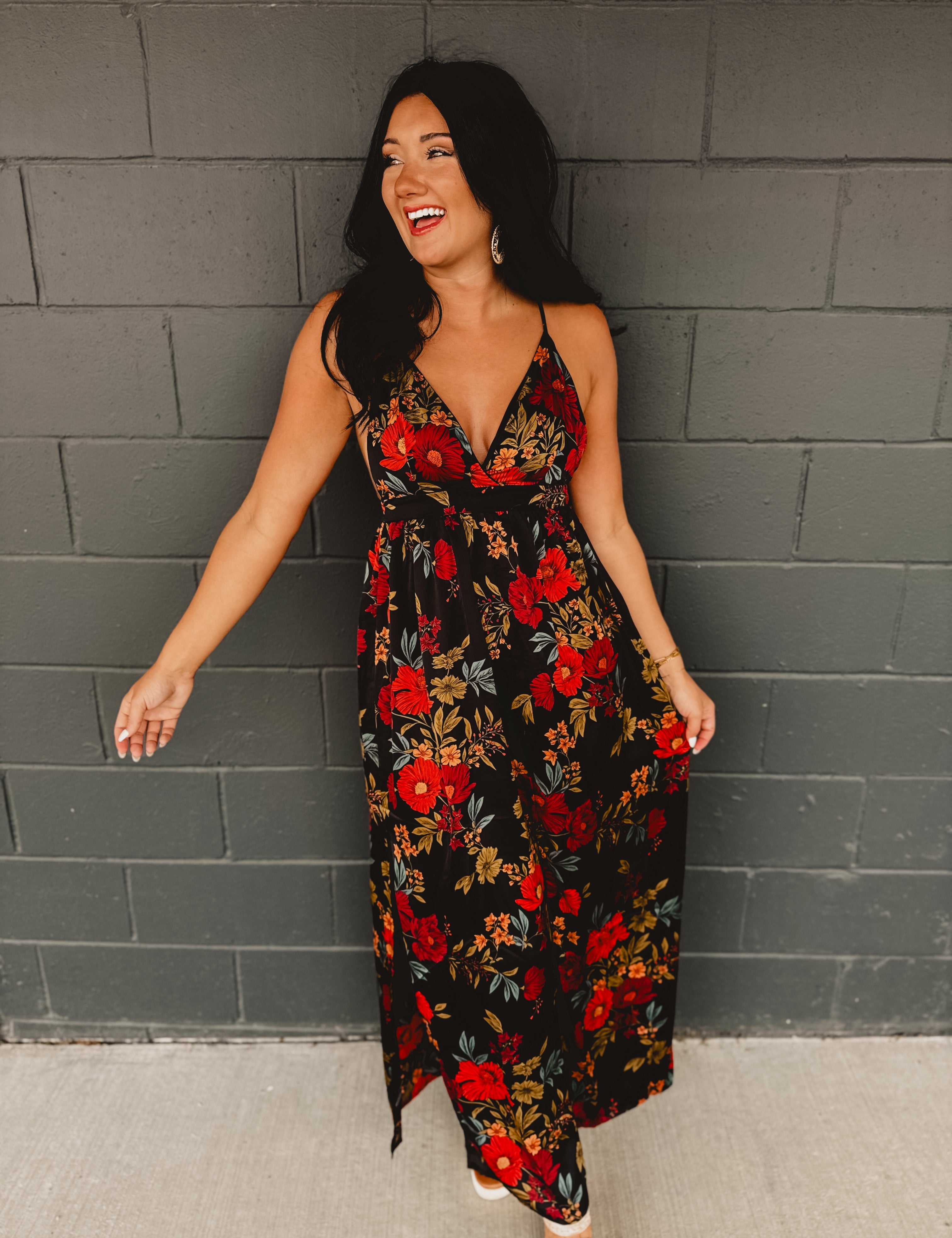 Black satin maxi dress with an empire waist and A-line skirt, featuring adjustable criss-cross back straps, a plunging neckline, and an open-back silhouette.