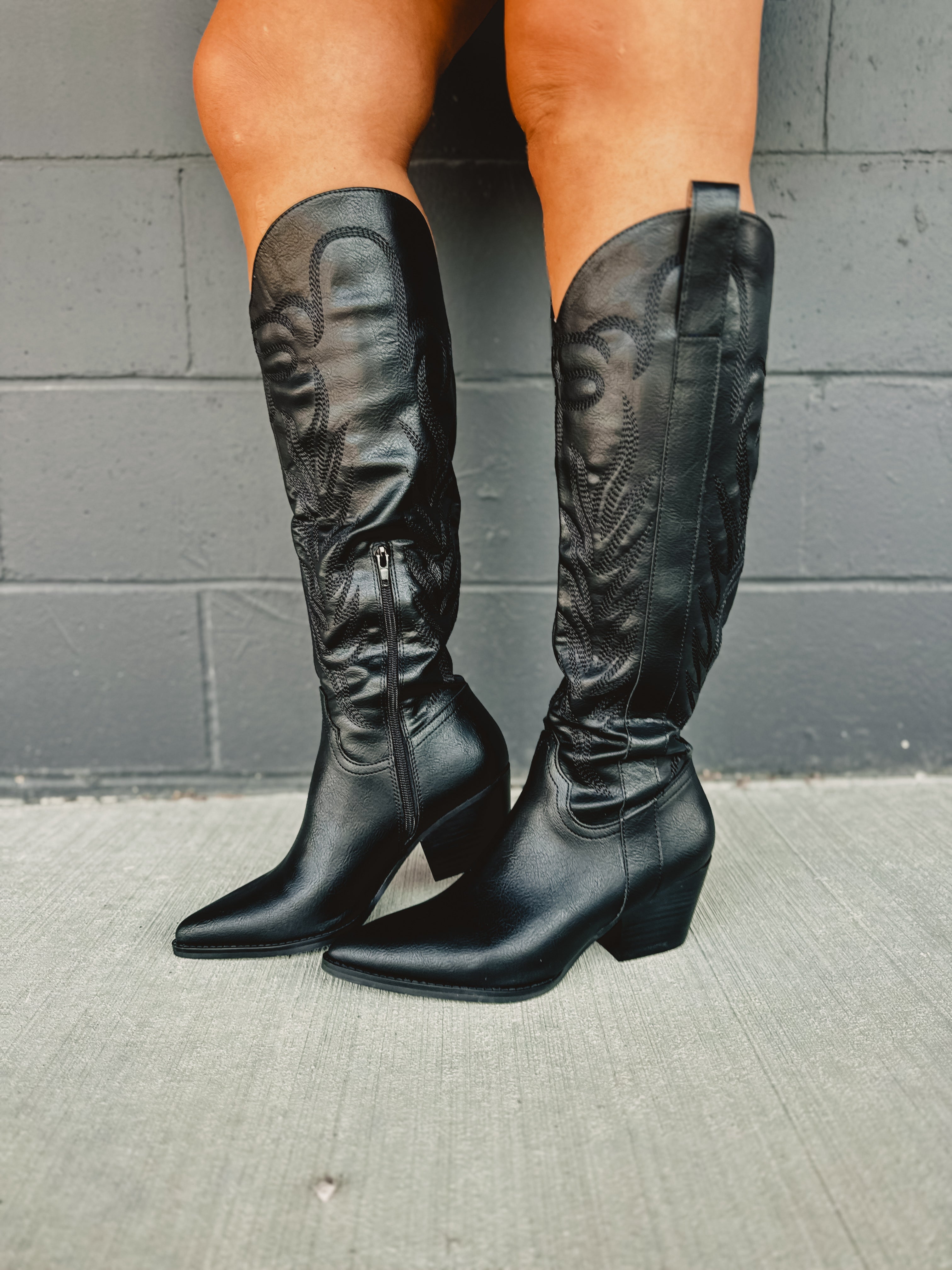 Zip-up below the knee tall black embroidered western boots with pointed toes and heels.