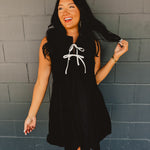 Sleeveless pleated black mini dress with white bow tie details.