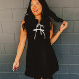Sleeveless pleated black mini dress with white bow tie details.