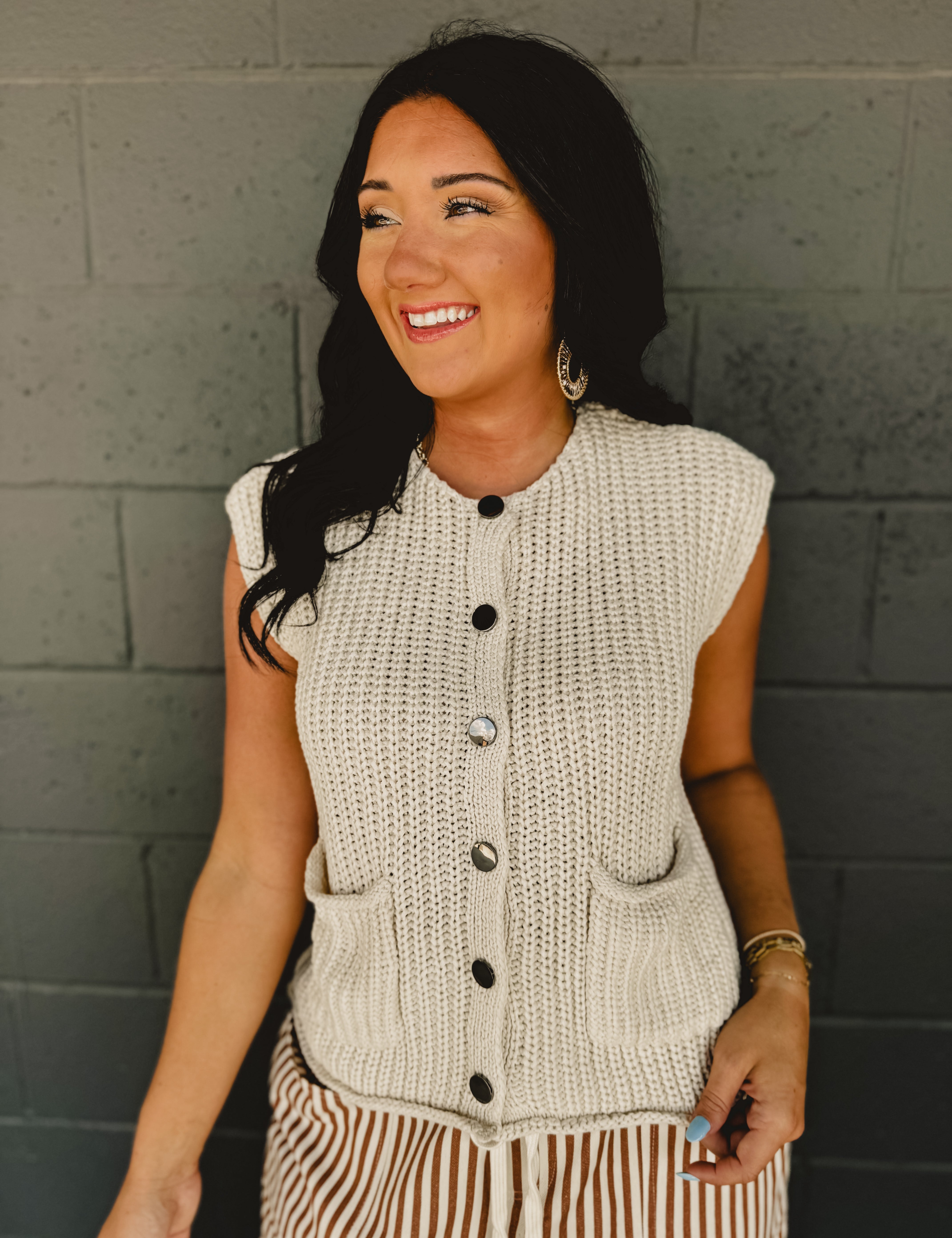 Sleeveless chunky button sweater vest with front pockets and a round neck in cream.