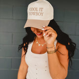 Two-toned one size baseball cap reading "Cool It Cowboy" in a cream and beige color.