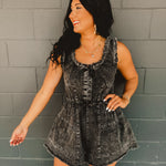 Frayed edge distressed sleeveless denim romper in acid wash black with metal clasp detail and cinching at waist.