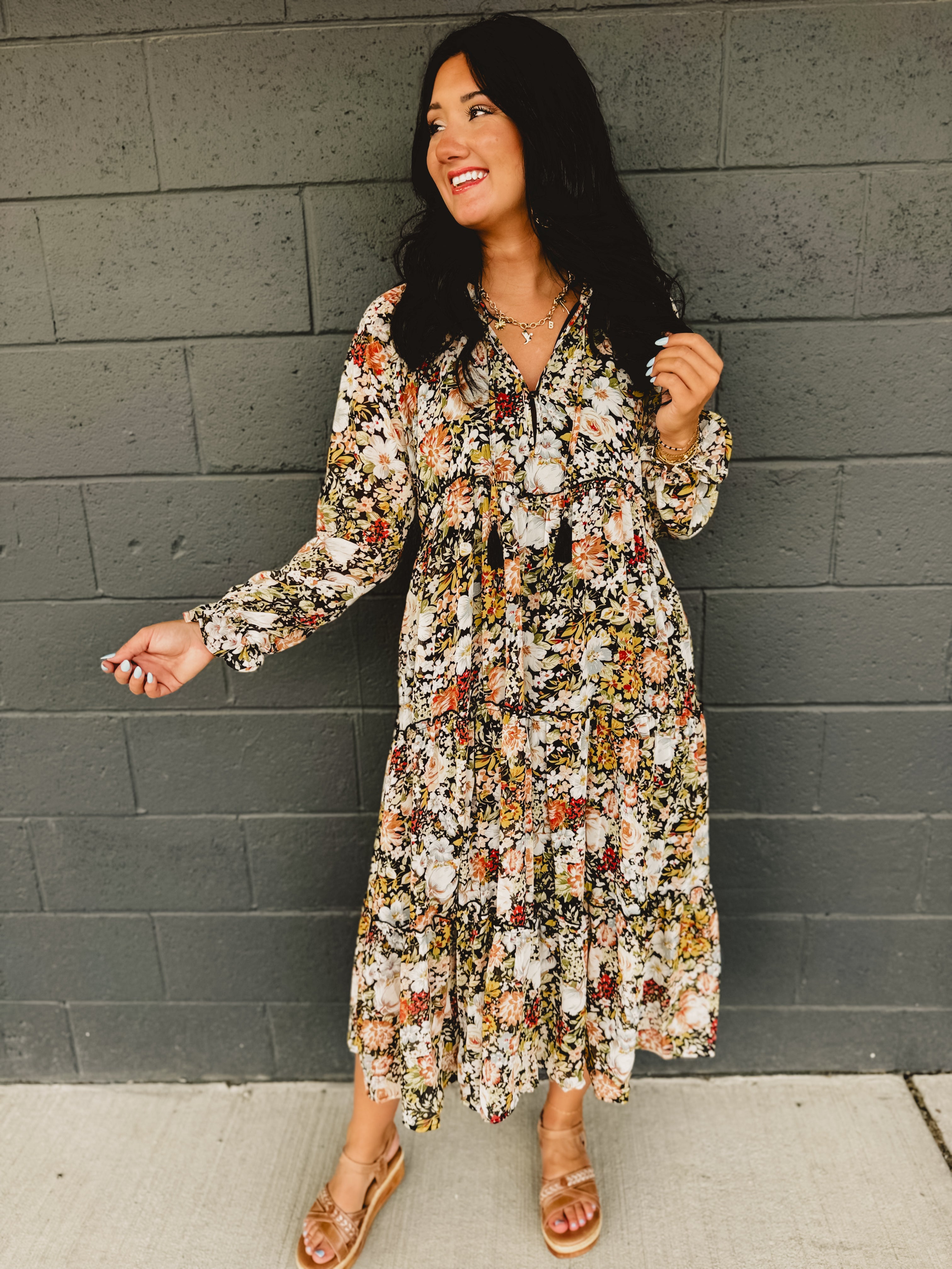 Long sleeve deep v-neck floral tiered midi dress with ruffle hems and tassels in black.