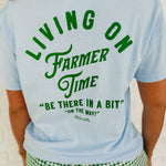 Light blue "Living On Farmer Time" short sleeved graphic tee with a round neck and green writing.