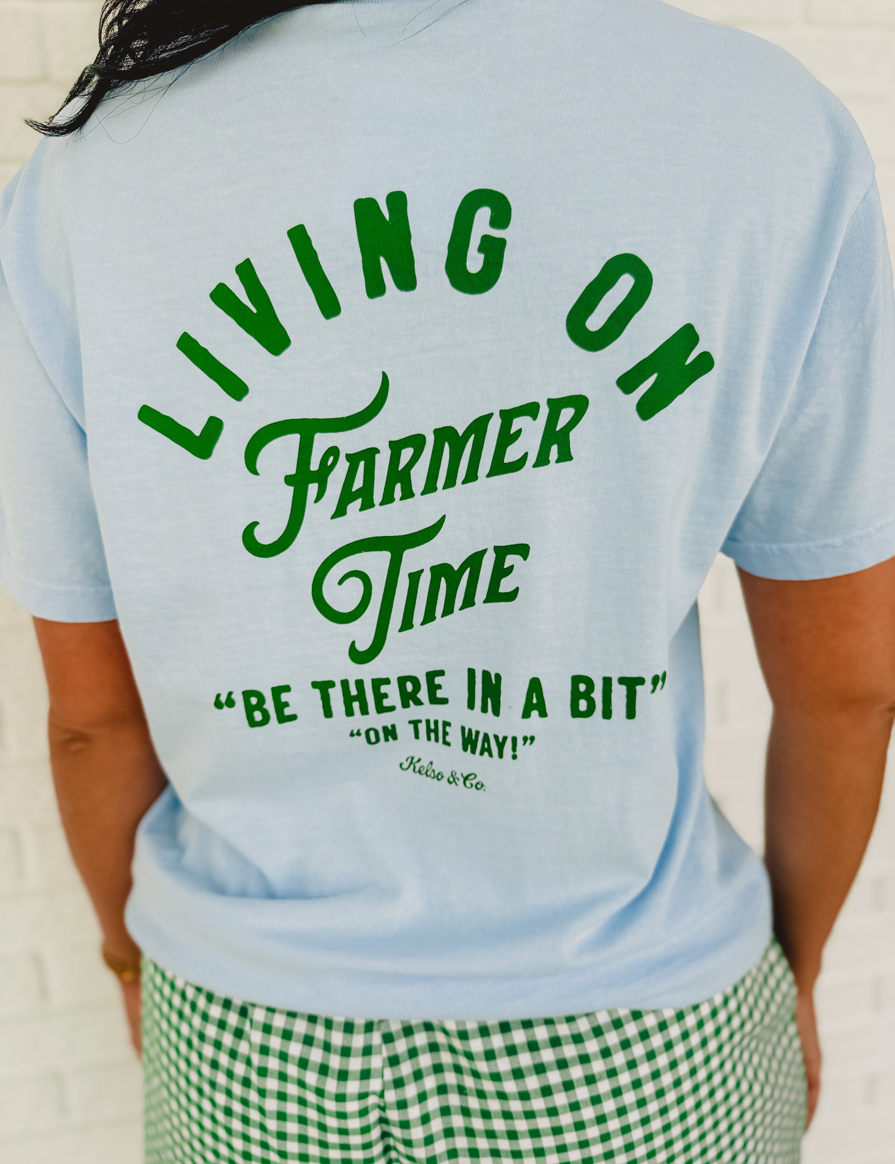 Light blue "Living On Farmer Time" short sleeved graphic tee with a round neck and green writing.