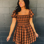 Orange and black plaid smocked mini dress with a square neckline and puff sleeves.