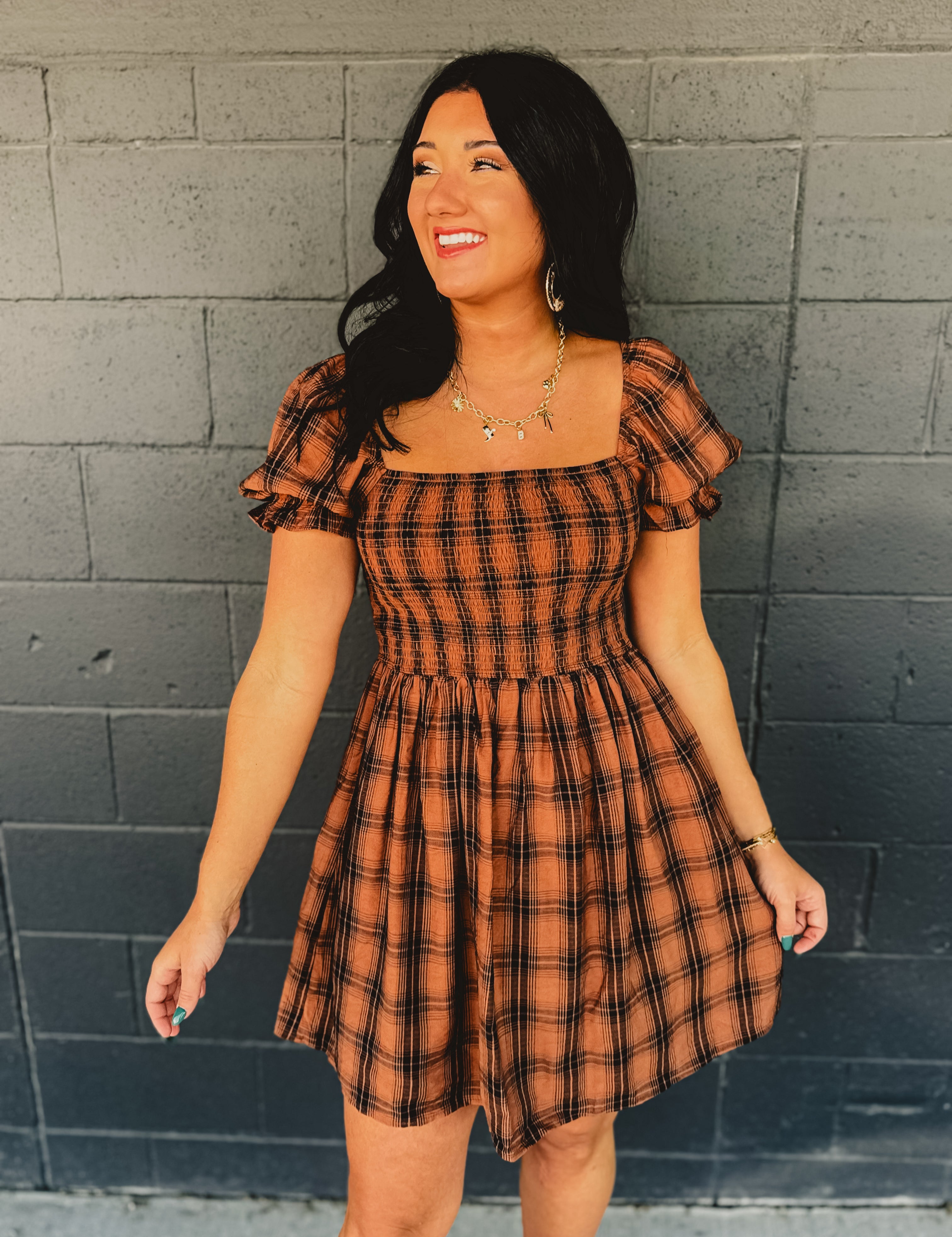 Orange and black plaid smocked mini dress with a square neckline and puff sleeves.