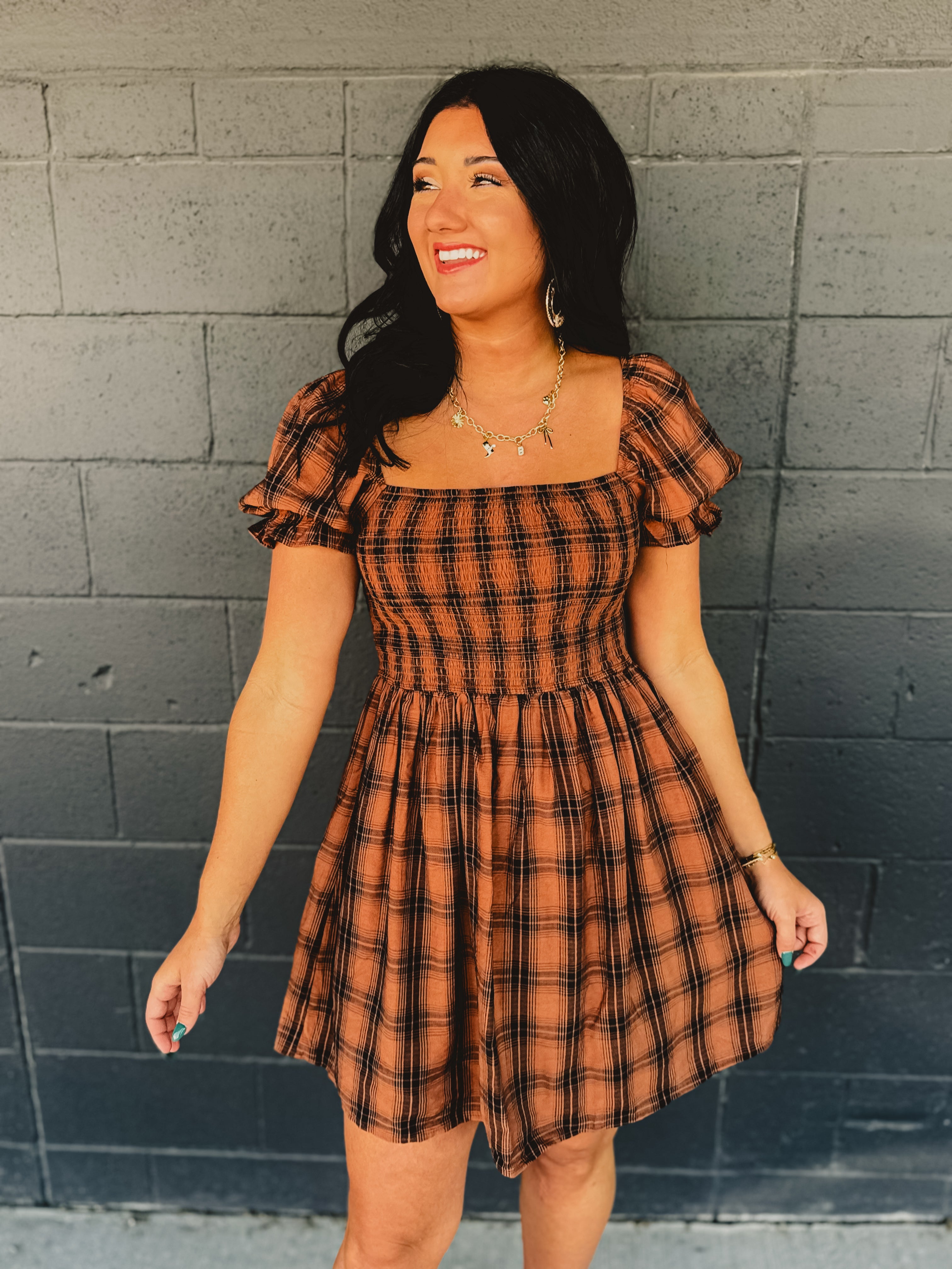 Orange and black plaid smocked mini dress with a square neckline and puff sleeves.