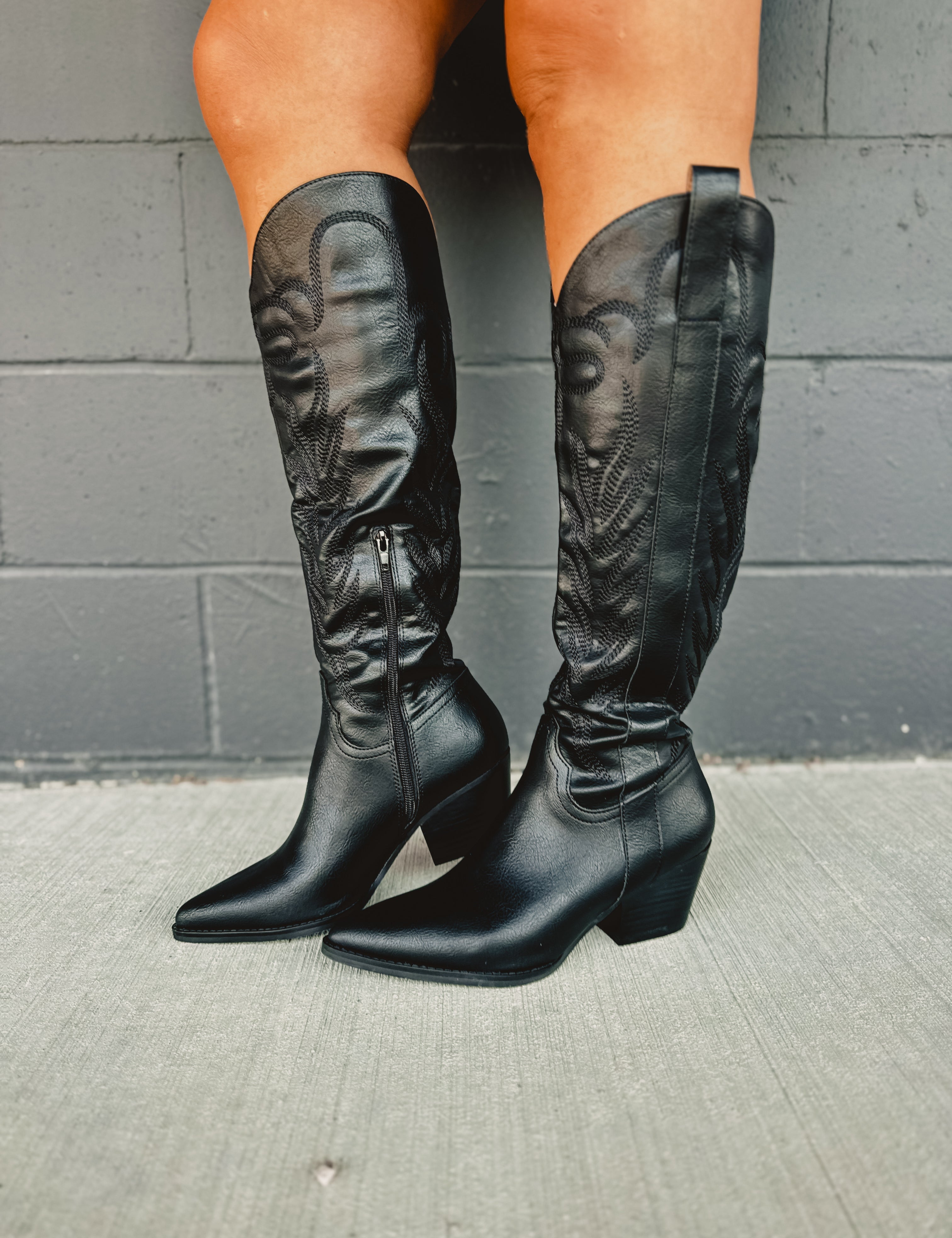 Zip-up below the knee tall black embroidered western boots with pointed toes and heels.